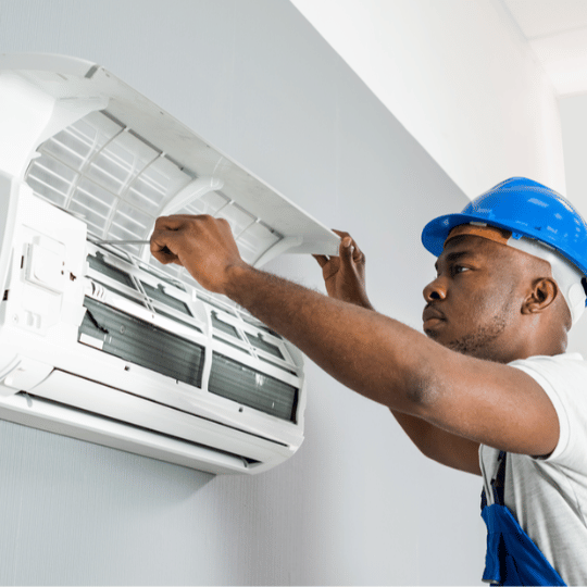 Technician in blue hard hat fixing air conditioner unit