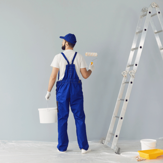 Painter in blue with roller beside ladder ready for wall painting