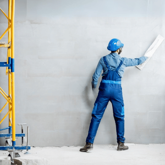 Worker in blue examining wall with blueprint