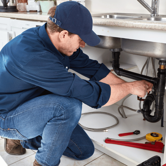 Plumber in dark blue fixing sink pipes