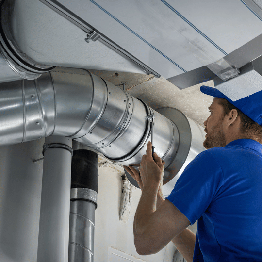 Technician in blue inspects HVAC ductwork